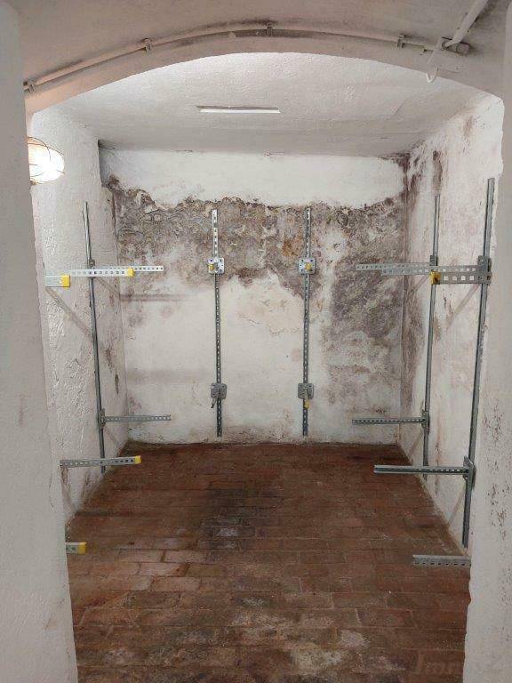 Kellerraum mit gewölbter Decke, Fliesenboden und Wandregalhalterungen.