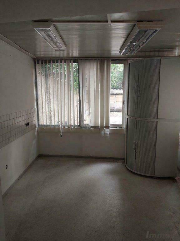 Büroraum mit großen Fenstern, vertikalen Jalousien und einem runden Aktenschrank.