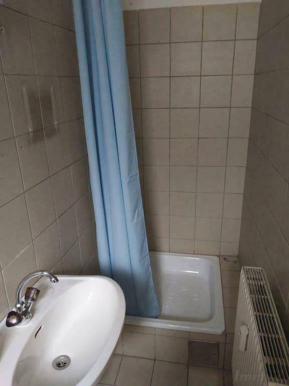 Kleines Badezimmer mit Duschwanne, Waschbecken und gefliesten Wänden.