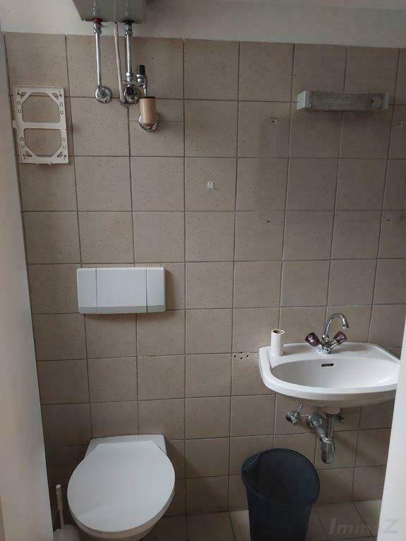 Geflieste Gästetoilette mit Waschbecken, WC und sichtbaren Wasserleitungen.