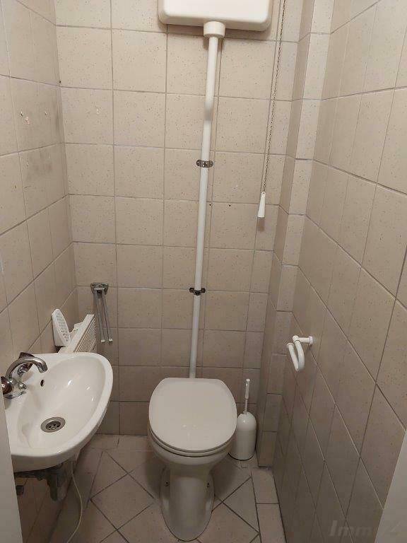 Einfache Gästetoilette mit Fliesen, Waschbecken und hochhängendem Spülkasten.