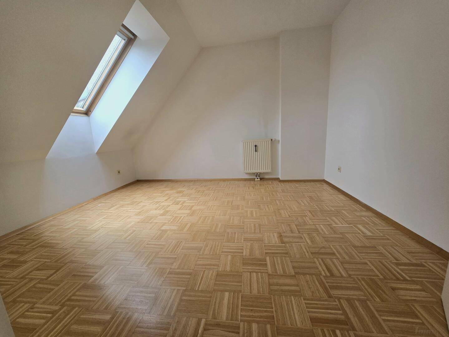 Geräumiges Zimmer mit Parkettboden, Dachschräge und einem Dachfenster.