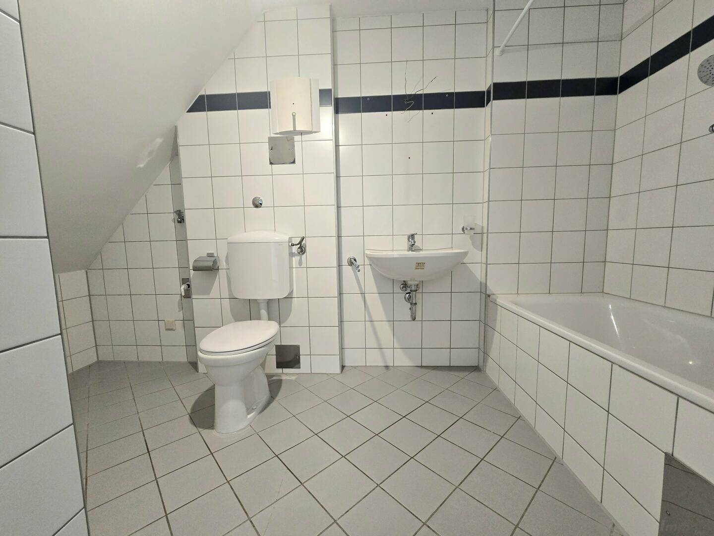 Badezimmer mit Badewanne, WC und Waschbecken, komplett gefliest.