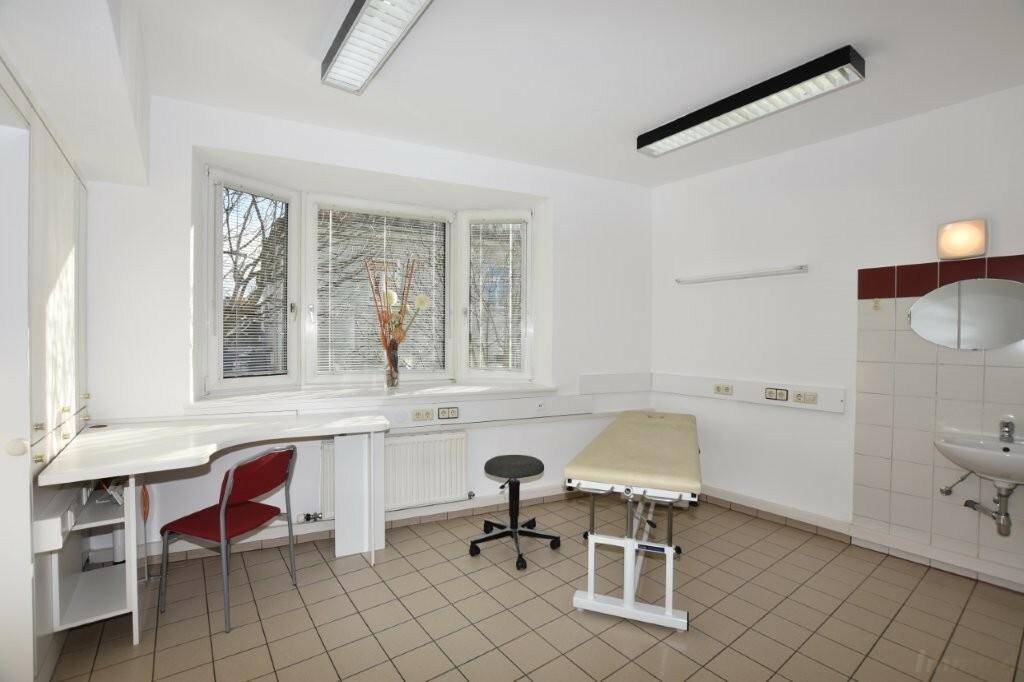 Heller Behandlungsraum mit Erkerfenster, Fliesenboden und integriertem Waschbeckenbereich.