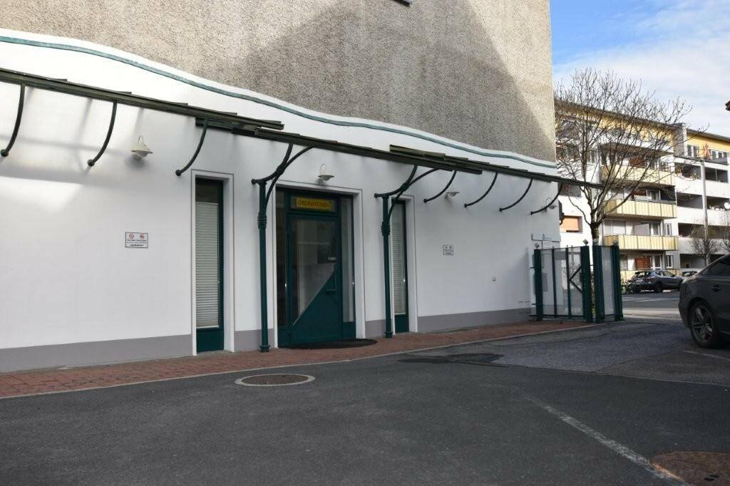 Eingangsbereich eines Geschäftsgebäudes mit grüner Tür, Vordach und angrenzenden Parkmöglichkeiten.