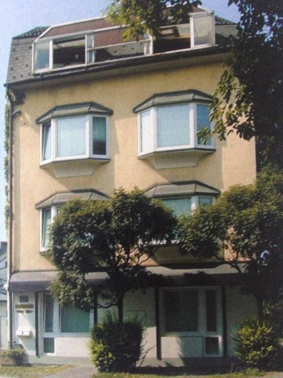 Mehrstöckiges Gebäude mit charakteristischen Erkerfenstern und Mansarddach in städtischer Umgebung.