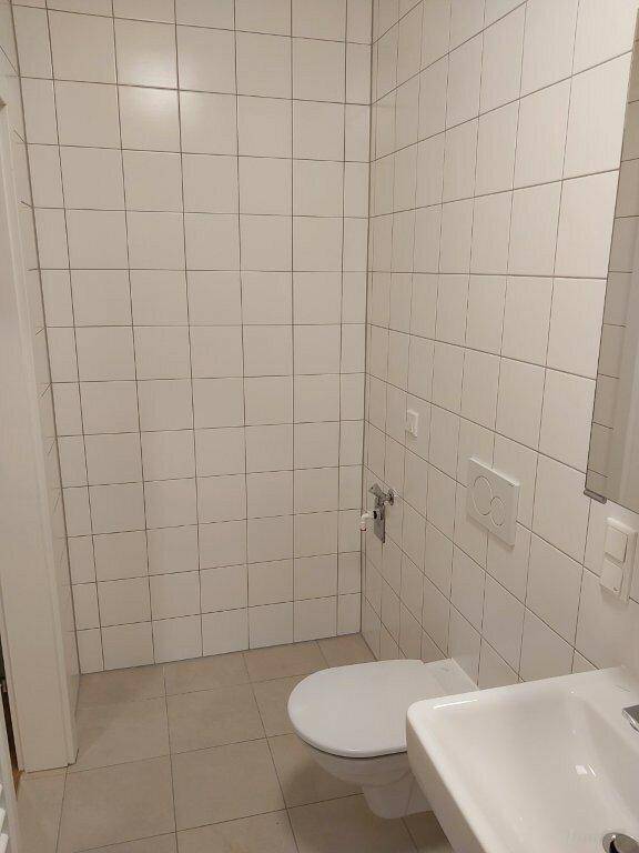 Gefliestes WC mit wandhängender Toilette und kleinem Waschbecken.