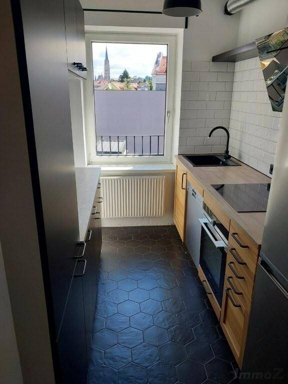 Schmale Küche mit modernen Geräten, dunklem Fliesenboden und Blick auf die Stadt.