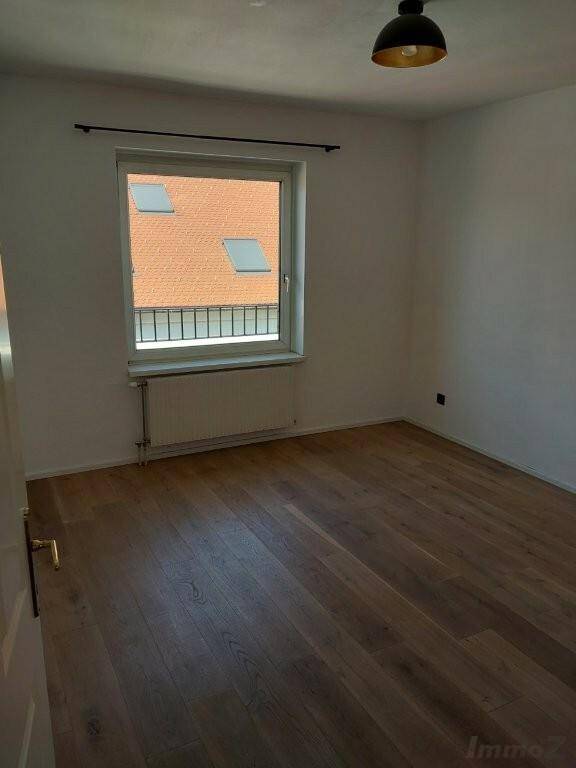 Leeres Schlafzimmer mit Holzboden, einem Fenster und Blick auf ein Dach.