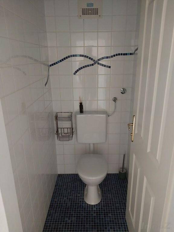 Separates WC mit Toilette, weißen Fliesen und dunklem Mosaikboden.