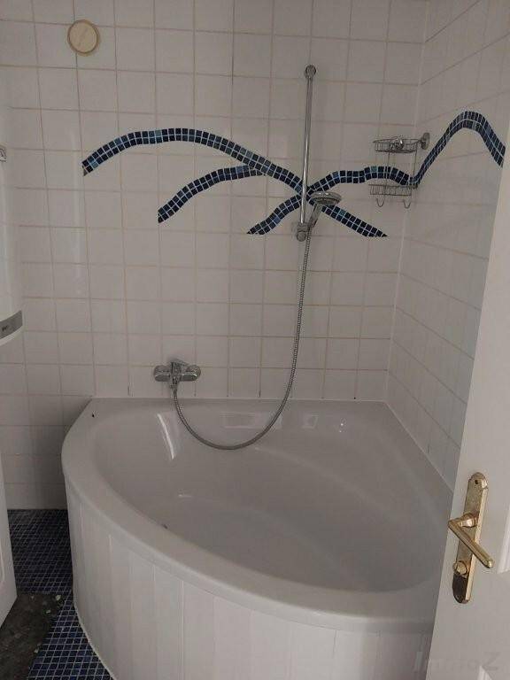 Eckbadewanne im Badezimmer mit weißen Fliesen und blauen Akzenten.