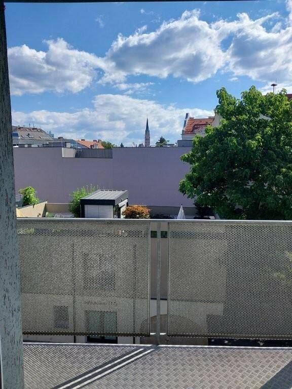 Balkon mit perforiertem Metallgeländer und Blick auf die Stadt und einen Kirchturm.