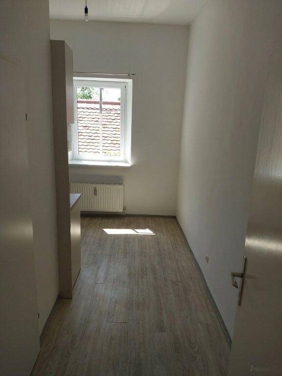 Heller, leerer Raum mit Laminatboden und Fensterblick auf ein Ziegeldach, gut gepflegt.