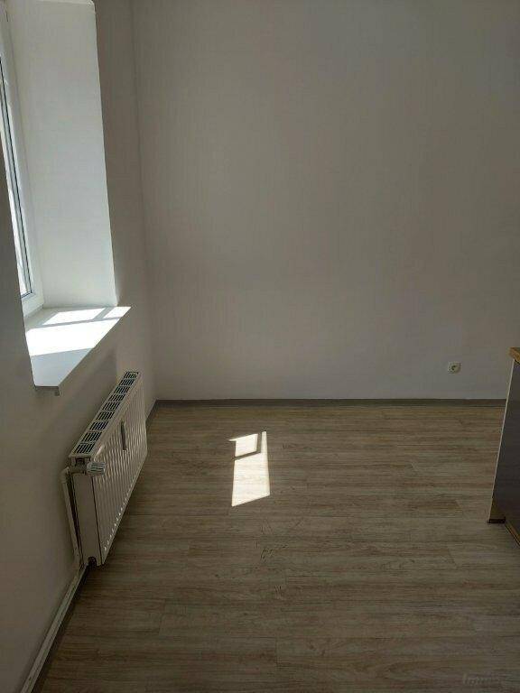 Leerer Raum mit Laminatboden, Heizkörper unter dem Fenster und viel Tageslicht, in gutem Zustand.