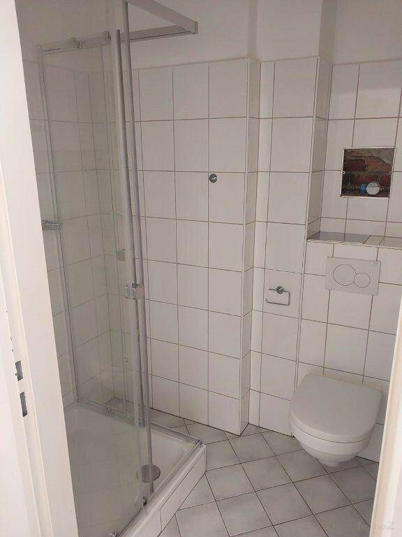 Gefliestes Badezimmer mit Duschkabine und wandhängendem WC in hellem, modernem Design.