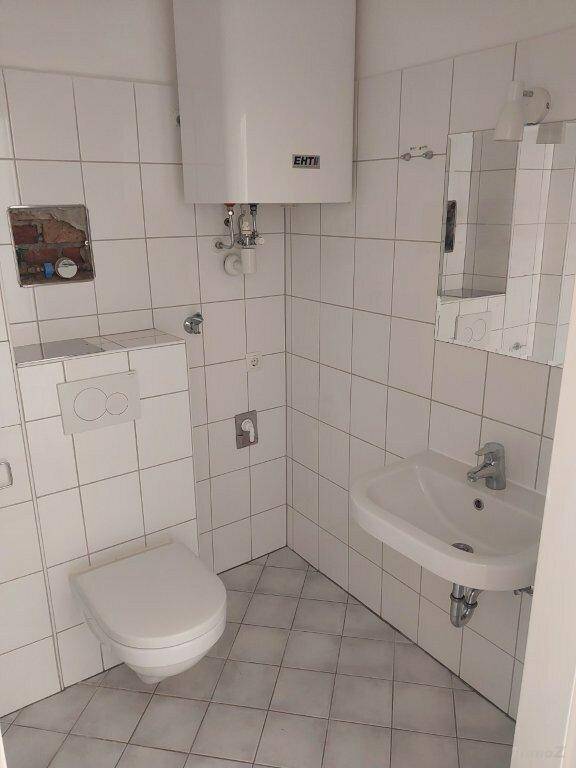 Kleines Badezimmer mit WC, Waschbecken, Boiler und weißen Wand- und Bodenfliesen, funktional ausgestattet.