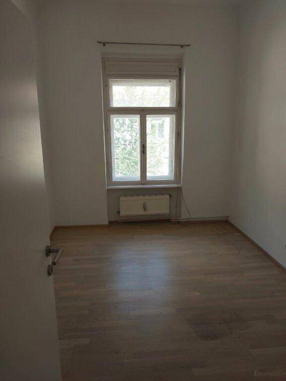 Heller, leerer Raum mit Holzfußboden und großem Fenster mit Rollladen, in gepflegtem Zustand.