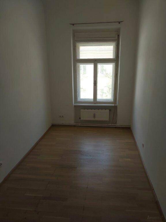 Leerer Raum mit Holzboden, Fenster mit Rollladen und heller Wandgestaltung, sauber und gepflegt.