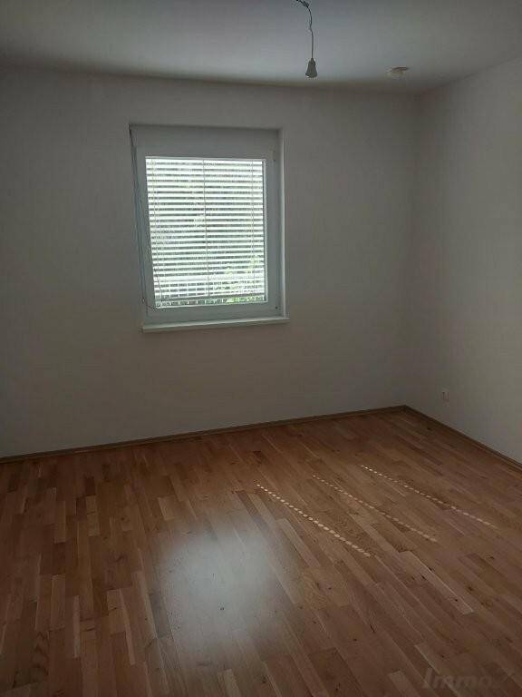 Leeres Zimmer mit Parkettboden und einem Fenster, das viel natürliches Licht hereinlässt.
