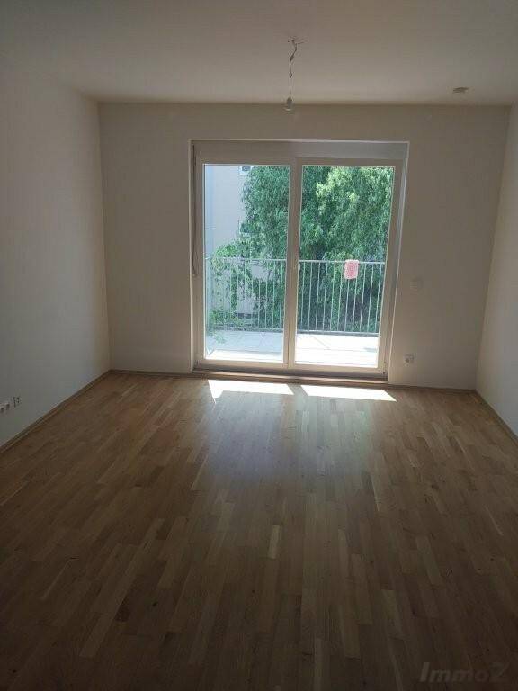 Helles Wohnzimmer mit Parkettboden und großen Fenstern, die Zugang zu einem französischen Balkon bieten.