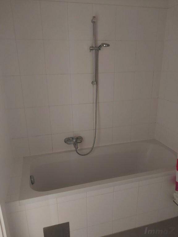 Badezimmer mit weißen Wandfliesen und einer Badewanne inklusive Duscharmatur.