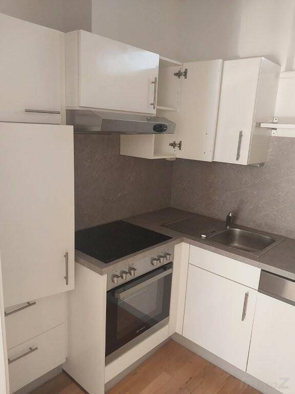 Moderne weiße Küche mit Einbaugeräten, Induktionskochfeld, Backofen und Dunstabzugshaube.