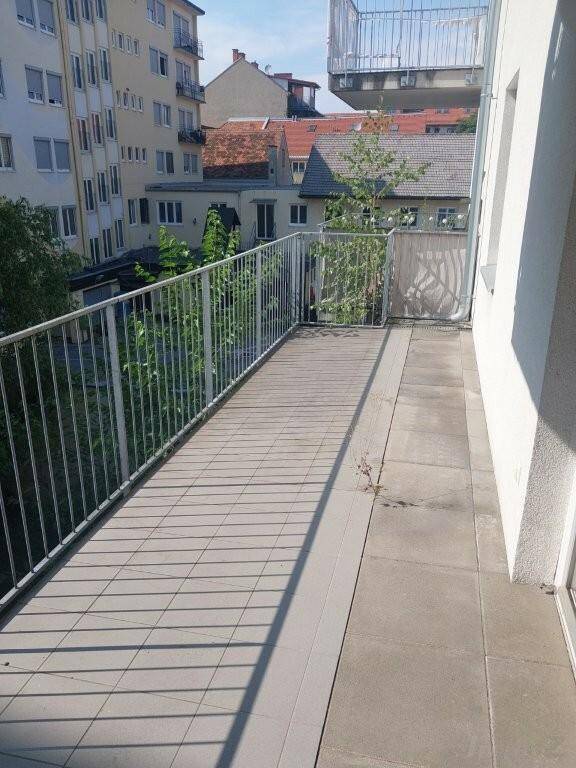Langer Balkon mit Metallgeländer und Blick auf umliegende Gebäude und Grünflächen.