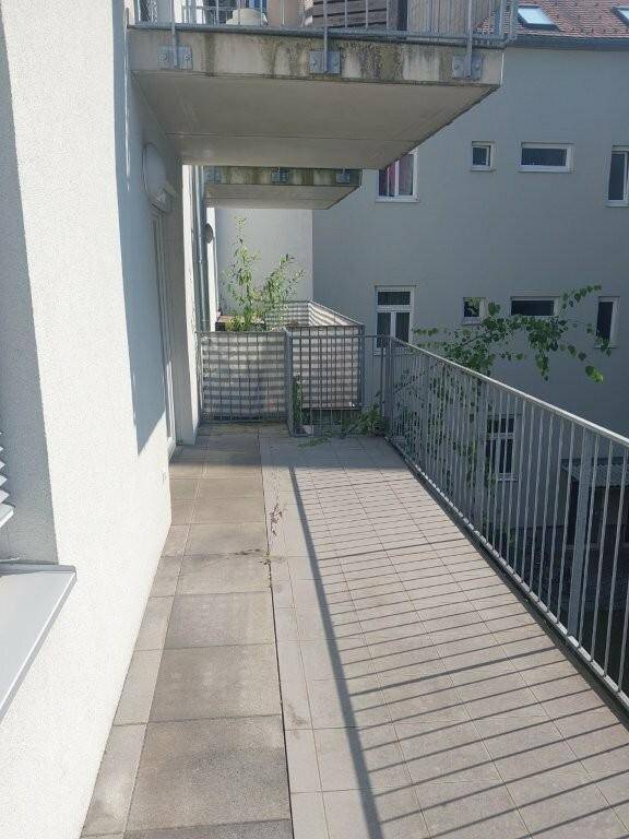 Geräumiger Balkon mit Metallgeländer und Ausblick auf die Nachbarschaft und Bäume.