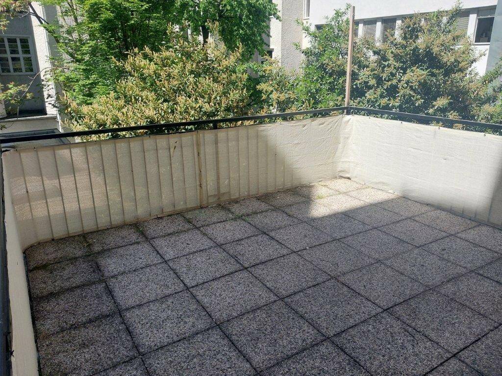 Geräumige geflieste Terrasse mit Blick auf grüne Bäume und umliegende Gebäude.