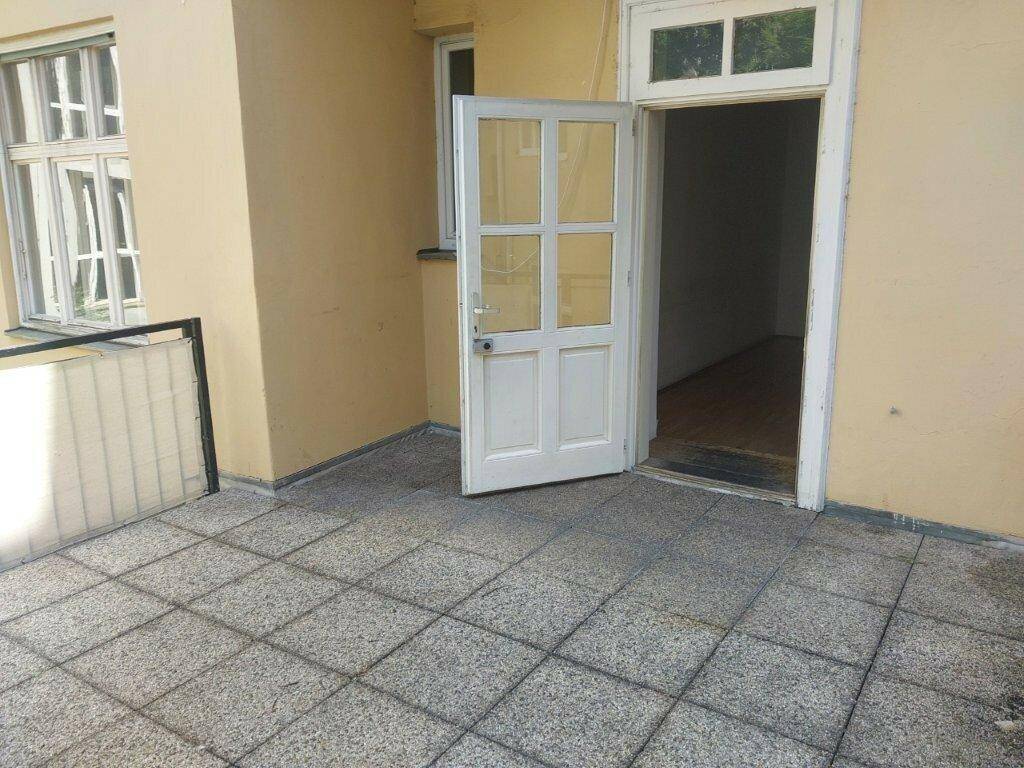 Zugang zur gefliesten Terrasse durch eine weiße Tür, umgeben von einer hellgelben Fassade.