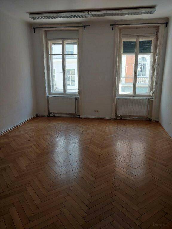 Helles Zimmer mit klassischem Fischgrätparkett und zwei großen Fenstern.