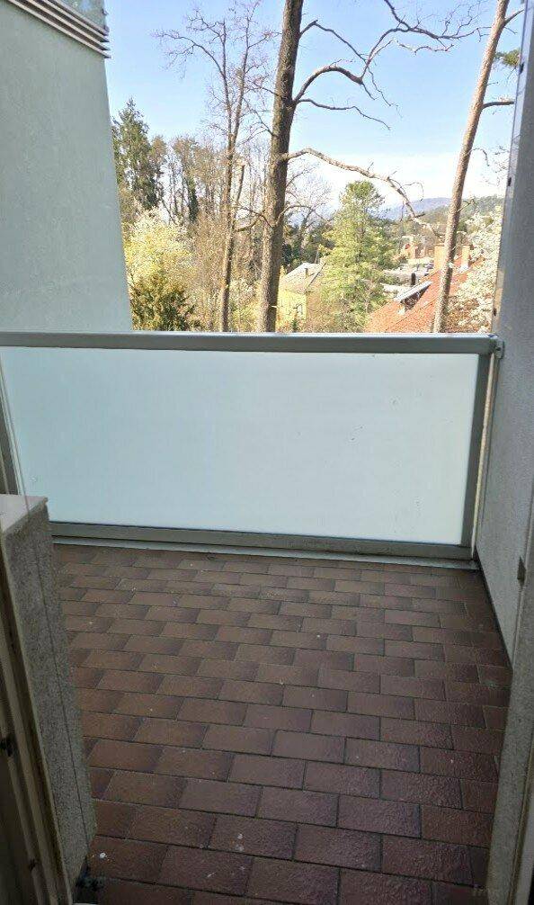 Überdachte Loggia mit Fliesenboden und Blick auf Bäume und die Umgebung.