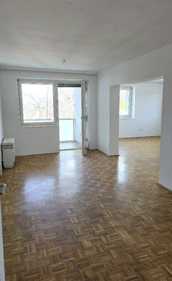 Geräumiges Wohnzimmer mit Parkettboden und Zugang zu einem Balkon oder einer Loggia.