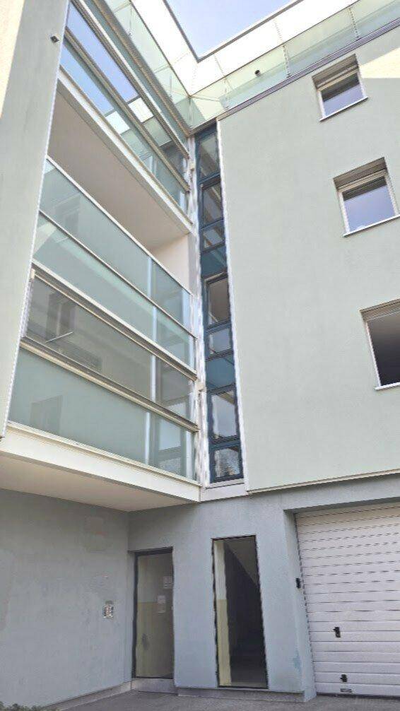 Moderne Gebäudefassade mit Glasbalkonen und einem sichtbaren Aufzugsschacht.