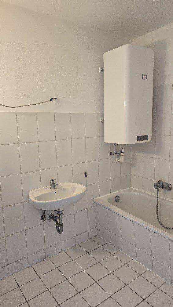 Badezimmer mit Badewanne, Waschbecken und weißen Fliesen, in gutem Zustand.