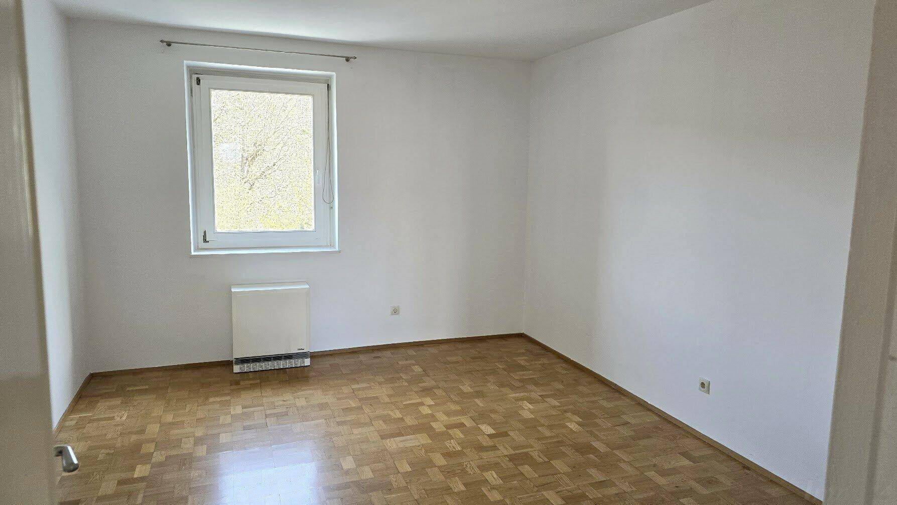 Unmöbliertes Zimmer mit Parkettboden und einem Fenster, das viel Licht spendet.