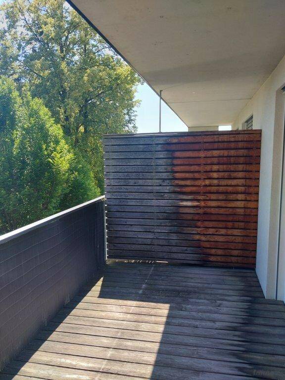 Balkon mit Holzboden und Sichtschutz, umgeben von grünen Bäumen.