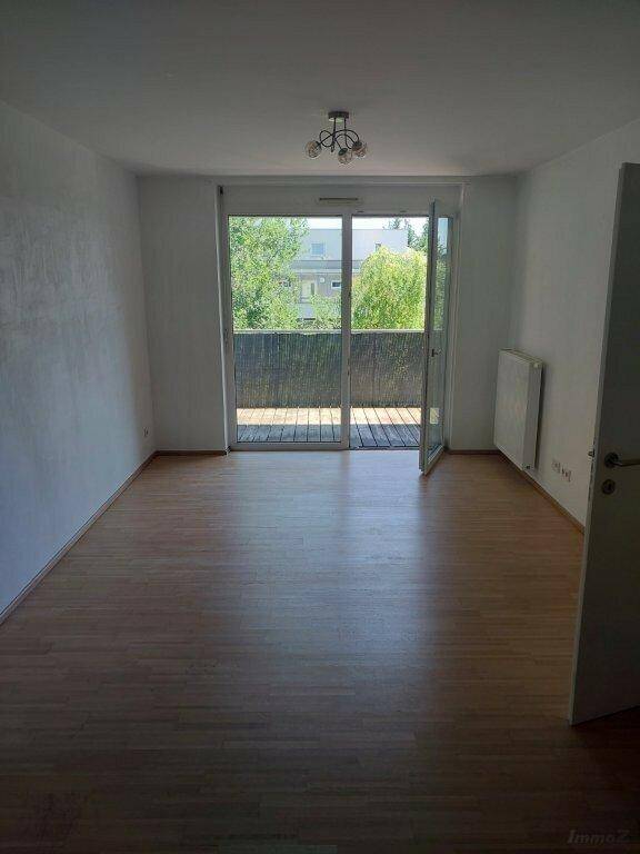Heller Wohnraum mit Laminatboden und Zugang zu einem Balkon mit Blick ins Grüne.