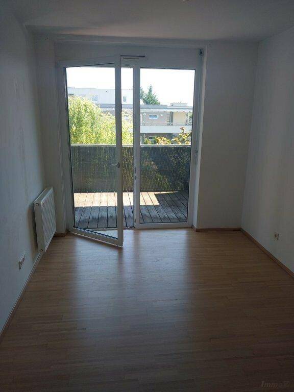Lichtdurchfluteter Raum mit Laminatboden und großen Fenstern, die Zugang zum Balkon bieten.