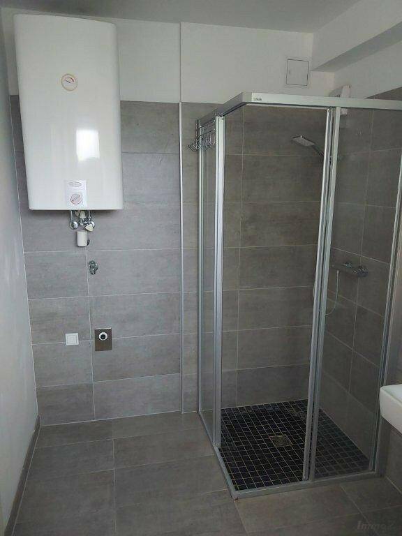 Badezimmer mit moderner Duschkabine, grauen Fliesen und einem Warmwasserboiler.
