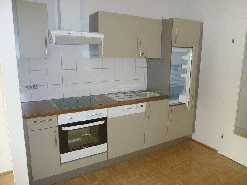 Funktionale Einbauküche mit hellen Schränken, Induktionskochfeld, Backofen und Kühlschrank.