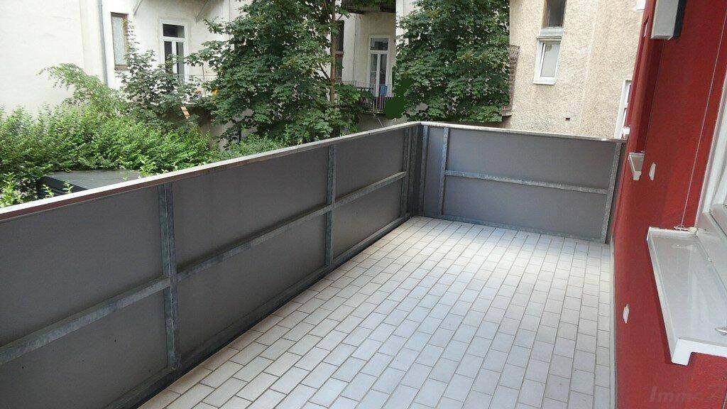 Geräumiger Balkon mit Fliesenboden und Blick auf den begrünten Innenhof.