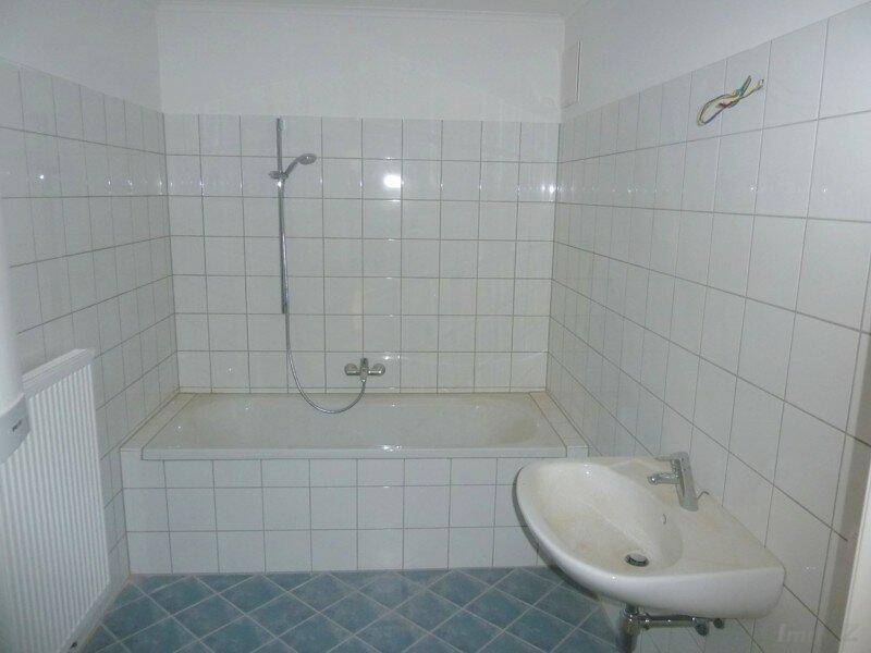 Badezimmer mit Badewanne, Duschfunktion, Waschbecken und weißen Wandfliesen im 80er-Jahre-Stil.