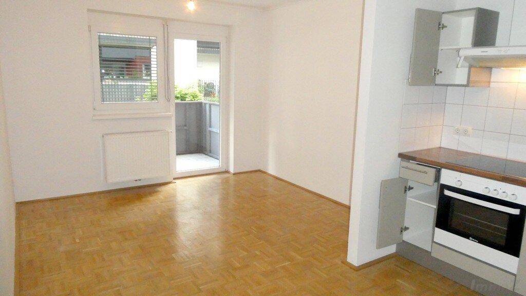 Heller Wohnbereich mit Parkettboden, Zugang zum Balkon und integrierter Küchenzeile.