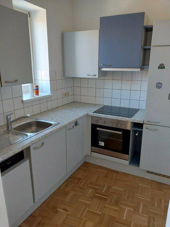 Kleine Küche mit hellgrauen Schränken, Fliesenrückwand und integrierten Geräten.
