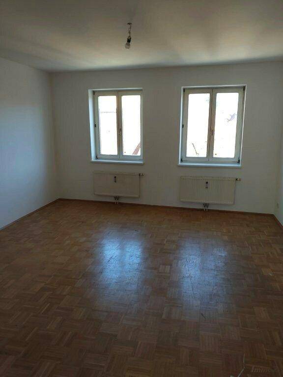 Leerer Raum mit Parkettboden und zwei Fenstern, bietet vielseitige Nutzungsmöglichkeiten.