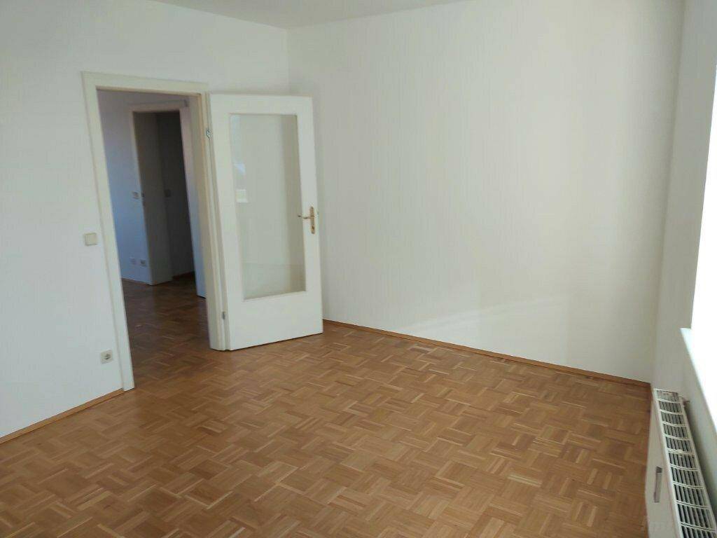 Geräumiger, heller Raum mit Parkettboden und Zugang zu weiteren Zimmern.