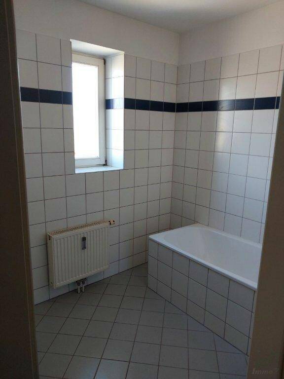 Badezimmer mit Badewanne, weißen Fliesen und Fenster für Tageslicht.