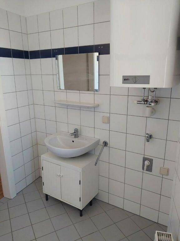 Badezimmer mit Waschbecken, Spiegel und Boiler, funktional und hell gefliest.