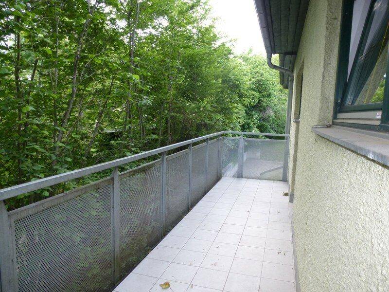 Langer Balkon mit Metallgeländer und Blick ins Grüne, umgeben von Bäumen.